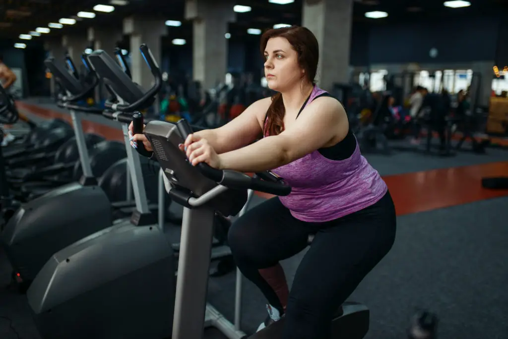 Overweight woman on exercise bike in gym